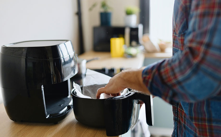 Papier do pieczenia w frytkownicy beztłuszczowej Mężczyzna przygotowujący jedzenie w frytkownicy beztłuszczowej – nowoczesne gotowanie