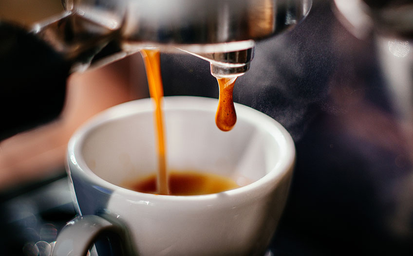 Kawa wpływa do białej filiżanki Strumień espresso wypływający z ekspresu do białej filiżanki w połowie wypełnionej kawą