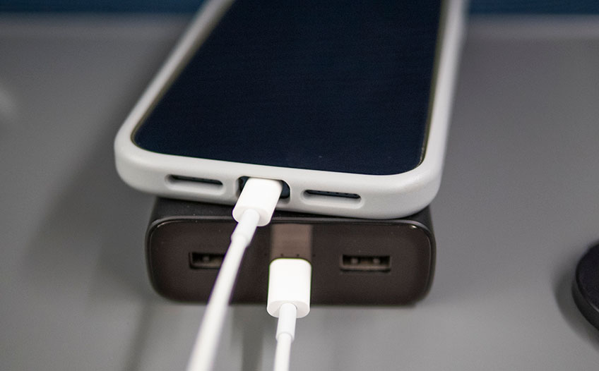 Telefon w białej obudowie leży na czarnym powerbanku Telefon w białej obudowie leży na czarnym powerbanku