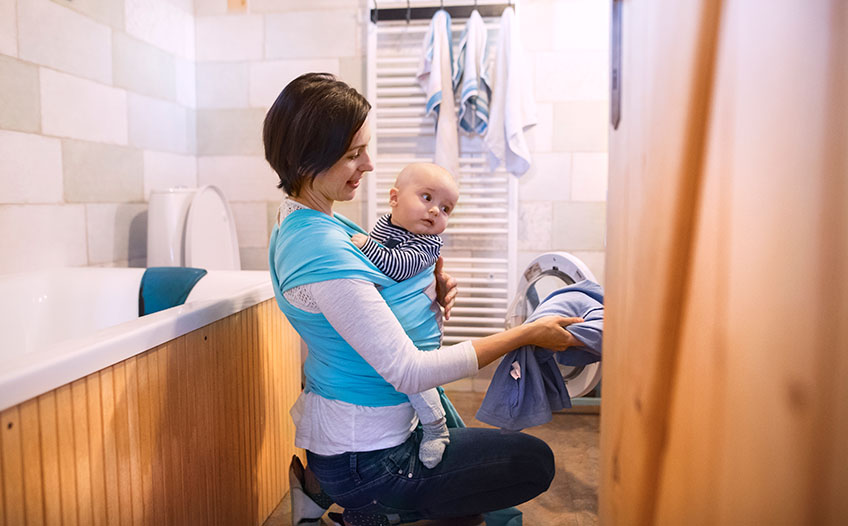 Matka z dzieckiem na ręku wyjmuje pranie w małej łazience