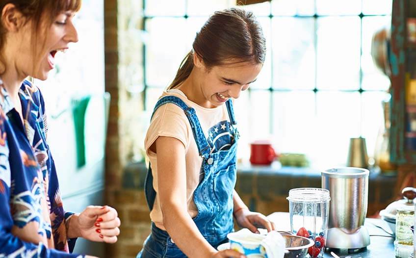 Roześmiana mama z córką przyrządzające deser owocowy w blenderze kielichowym Roześmiana mama z córką przyrządzające deser owocowy w blenderze kielichowym