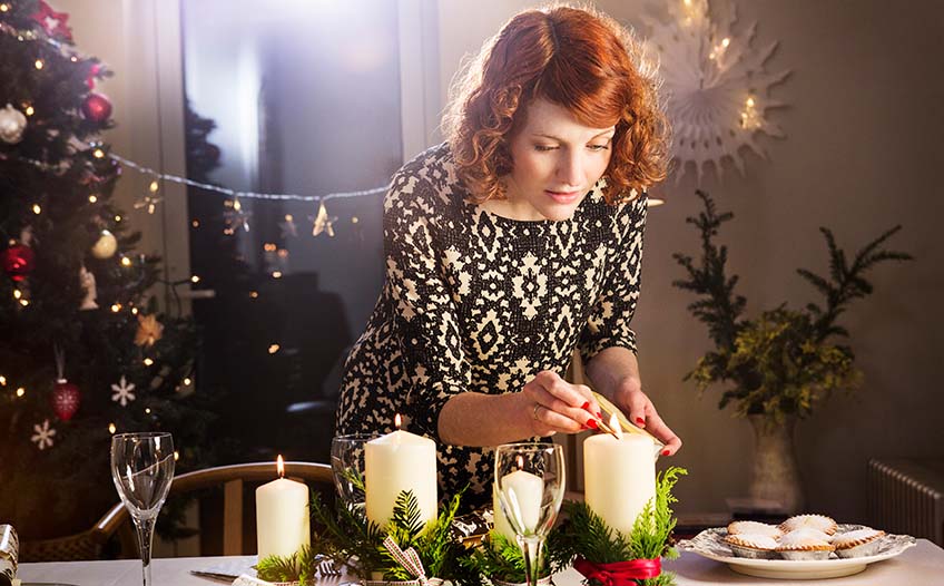 Kobieta zapala świece na świątecznym stole