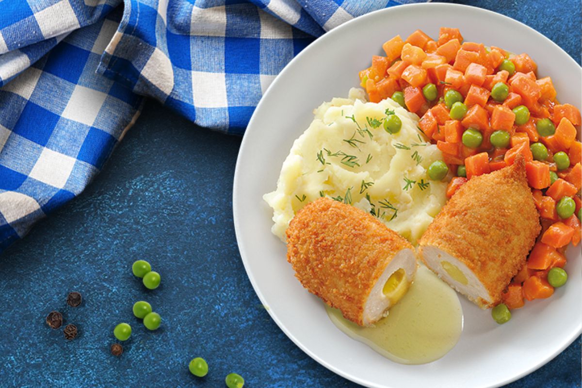 De volaille – klasyczne danie obiadowe. Panierowany kotlet de volaille z masłem, podany z puree ziemniaczanym i groszkiem z marchewką.
