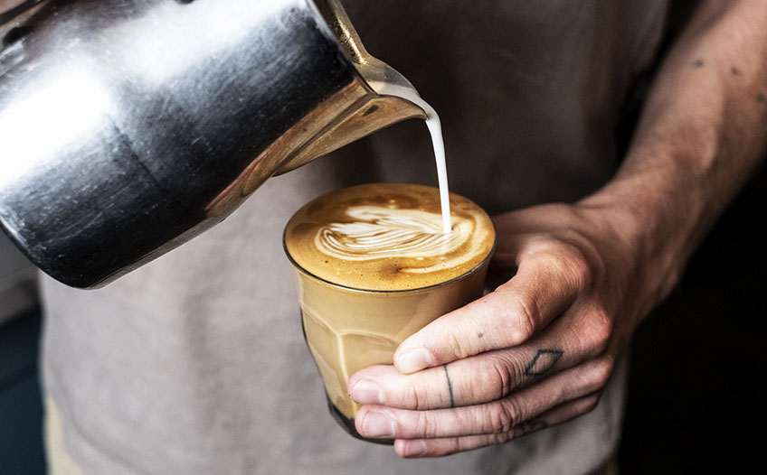 Sztuka tworzenia latte art – wlewanie mleka do espresso. Barista wlewa spienione mleko do filiżanki z kawą.