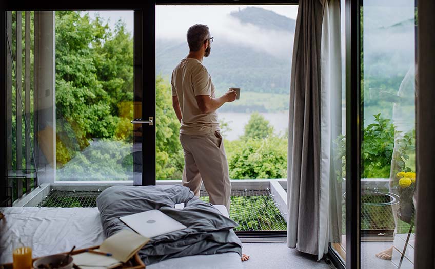 Mężczyzna w średnim wieku spogląda przez okno w sypialni
