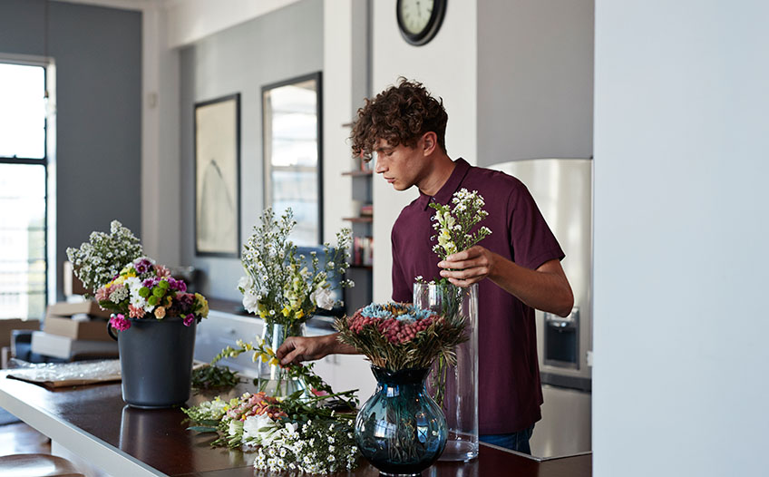 Młody chłopak w salonie układa kwiaty w bukiet do wazonu